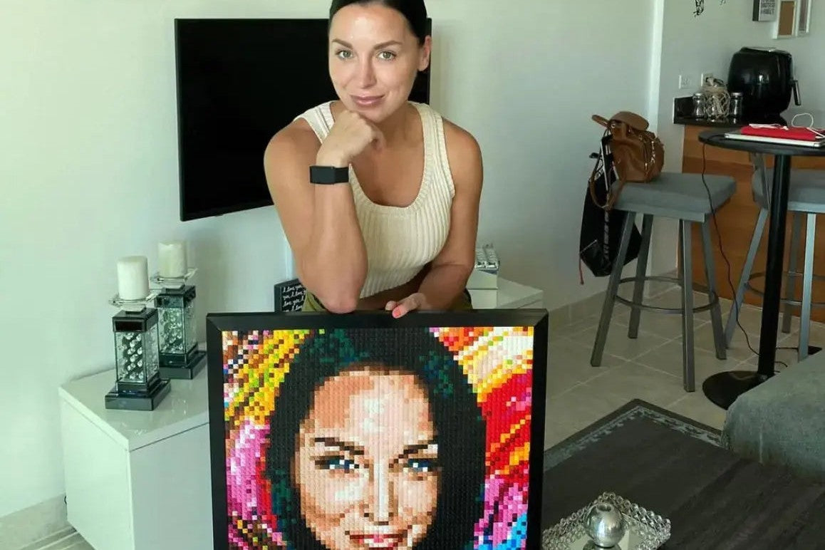 A woman at home with a finished, framed brick mosaic of her own portrait