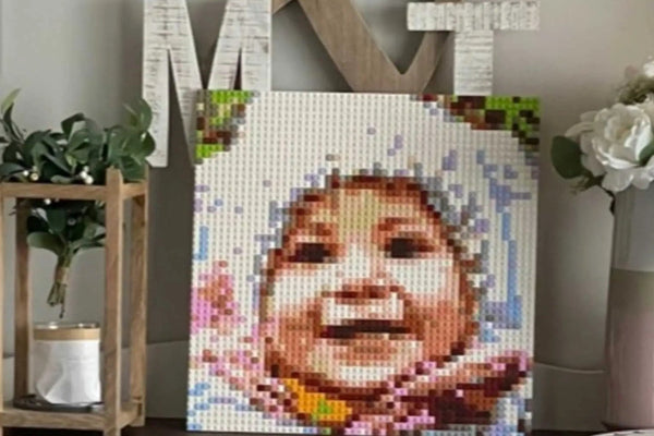 A finished brick mosaic of a smiling baby in a winter hat, displayed on a dresser at home
